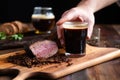 hand opening a stout next to beef brisket on a board