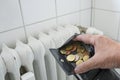 Hand is opening a wallet with few coins in front of an old, inefficient heater in a rental apartment, energy crises is increasing