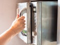 Hand opens an old steel microwave oven at home