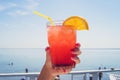 Hand with orange coctail glass over turquoise lagoon exotic bay. Lifestyle summertime vacation concept. girl holding a glass of