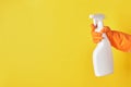 A hand in a orange glove holds a white spray bottle of cleaning fluid on a yellow background Royalty Free Stock Photo
