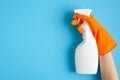 Hand in orange rubber glove holding plastic spray bottle with cleaning detergent on a blue background Royalty Free Stock Photo
