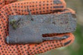 a hand in an orange work glove holds an old brown rusty iron door hinge Royalty Free Stock Photo