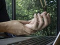 Hand pain from using a computer. Close-up man holding his wrist near laptop on green nature background, working at home. Royalty Free Stock Photo