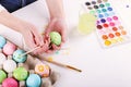 Hand painted Easter eggs, paints and brushes on a white table. Preparation for the holiday. Girls hands draw a pattern