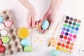 Hand painted Easter eggs, paints and brushes on a white table. Preparation for the holiday. Girls hands draw a pattern