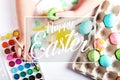 Kid hand painted boiled Easter eggs, paints and brushes on a white table. Preparation for the holiday. Girls hands draw a pattern