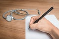 Hand with pen over blank paper form with stethoscope and pills Royalty Free Stock Photo