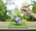 Hand with pencil drawing planet and tree from an open book on wooden table over green tree blur background, ecological concept Royalty Free Stock Photo
