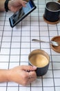 Hand of people holding a black cup of latte coffee and using smartphone on white grid table background , coffee break time Royalty Free Stock Photo