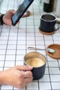 Hand of people holding a black cup of latte coffee and using smartphone on white grid table background , coffee break time relax Royalty Free Stock Photo