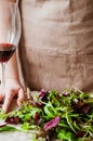 Hand of a person in an apron, who cooks and sorts greenery, lies on the table near a glass of red wine Royalty Free Stock Photo