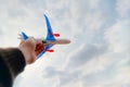 The hand of the person holds the toy plane against the blue sky and white clouds. The concept of freedom, flight and travel