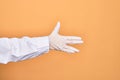 Hand of a person wearing medical surgical glove doing Star Trek salutation over isolated yellow background