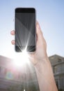 Hand with phone against blurry building with flare Royalty Free Stock Photo