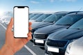 Hand with phone on a background of rows of cars.