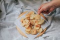 Hand pick up pieces of fresh homemade deep fried crispy potato chips on a wooden tray, top view. Salty crisps scattered on a tabl