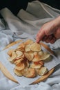 Hand pick up pieces of fresh homemade deep fried crispy  potato chips on a wooden tray, top view. Salty crisps scattered on a tabl Royalty Free Stock Photo