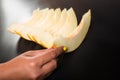 Hand picking piece of melon. Sliced honeydew on black table. Female hand holding tropical fruit Royalty Free Stock Photo