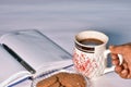 A hand is picking up a cup of black tea from the study table to enjoy alongside a plate of cookies and a diary with a pen Royalty Free Stock Photo