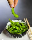Hand picking up an edamame bean from a bowl. Fresh green soybeans in a bowl with chopsticks