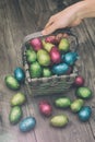 Hand picking up a straw basket filled with Easter chocolate eggs wrapped in colorful tinfoil Royalty Free Stock Photo