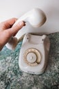 A hand picks up the phone on an old analog white Soviet telephone
