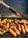 Hand with pincer placing a sausage on the grill