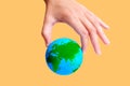 Hand Pinch-Holding a Green and Blue Globe on Yellow Royalty Free Stock Photo