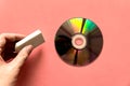 Hand pinching rubber over light reflected compact discs CD or digital versatile disc DVD on the pink paper background.