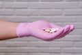 Hand in pink medical glove with a handful of pills on white brick wall background, close up Royalty Free Stock Photo