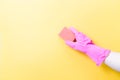 hand in pink rubber glove holds orange sponge for washing dishes and cleaning, yellow background copy space Royalty Free Stock Photo