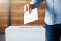A hand places a vote in the ballot box, a symbol of democracy