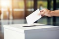 A hand places a vote in the ballot box, a symbol of democracy