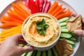 hand placing bell pepper slice into platter of hummus