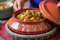 hand placing a ceramic lid on a colorful lamb tagine