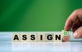 Hand placing a check mark block next to the word ASSIGN, with a blurred green background. This image symbolizes task ass Royalty Free Stock Photo
