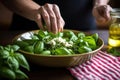 hand placing decorative basil leaves on salad top