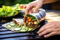 hand placing a finished bbq veggie wrap on a platter with barbecue smoke behind