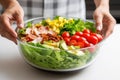 a hand placing fresh lettuce in a bowl as the first layer of a cobb salad