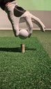 Hand placing a golf ball on a tee during an indoor practice session at a golf facility concept Royalty Free Stock Photo