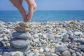 Hand placing the last pebble of a stacked tower on the sea side Royalty Free Stock Photo