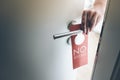Hand placing red do not disturb sign on handle of hotel room door Royalty Free Stock Photo