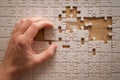 A hand is placing or removing a white jigsaw puzzle piece on a flat surface. Royalty Free Stock Photo
