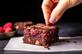 hand placing a single raspberry on top of a square of brownie