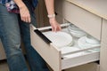 Hand placing stack of white ceramic plates inside kitchen drawer with bowls Royalty Free Stock Photo