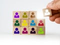 A hand placing a wooden block with colorful people icon onto many others, putting the right man into the right position, HR Royalty Free Stock Photo