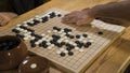 Hand playing black and white stone pieces on Chinese Go or Weiqi game board. Indoor activity with artificial light.