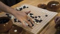 Hand playing black and white stone pieces on Chinese Go or Weiqi game board. Indoor activity with artificial light.