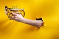 Hand playing horn through a torn hole in yellow paper background Royalty Free Stock Photo